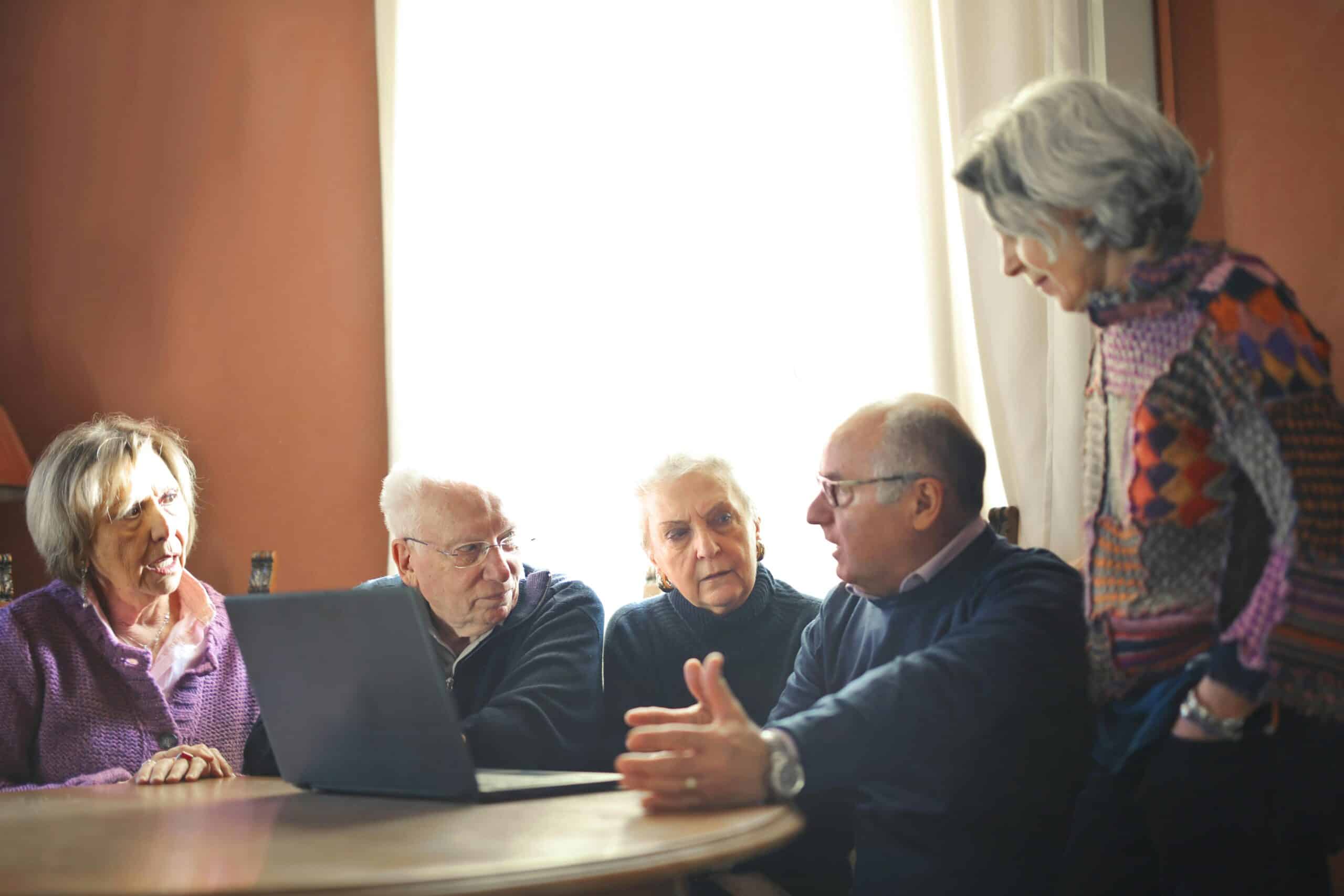 Ryhmä senioireita pöydän äärellä tietokone edessään keskustelevat yhdessä