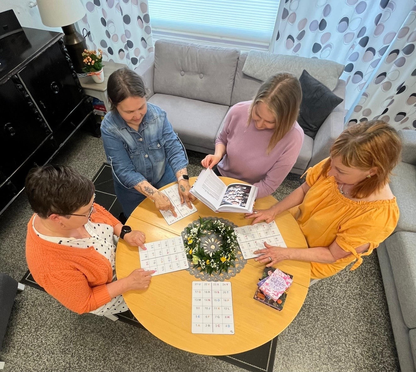 neljä naista istuu pöydän ympärillä ja pelaa peliä