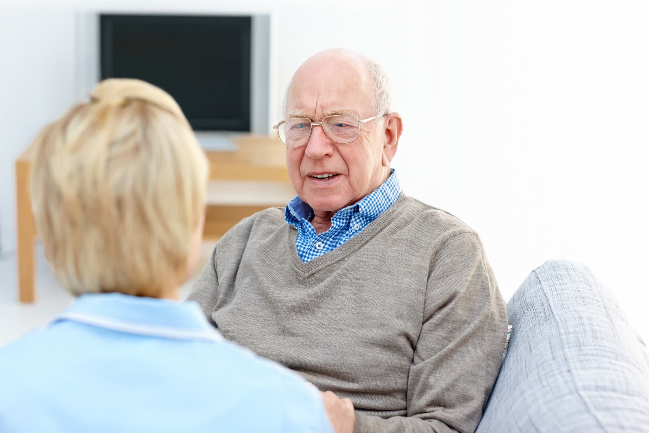 Vanhempi mies keskustelee hoitajan kanssa. He istuvat miehen kotona sohvalla.