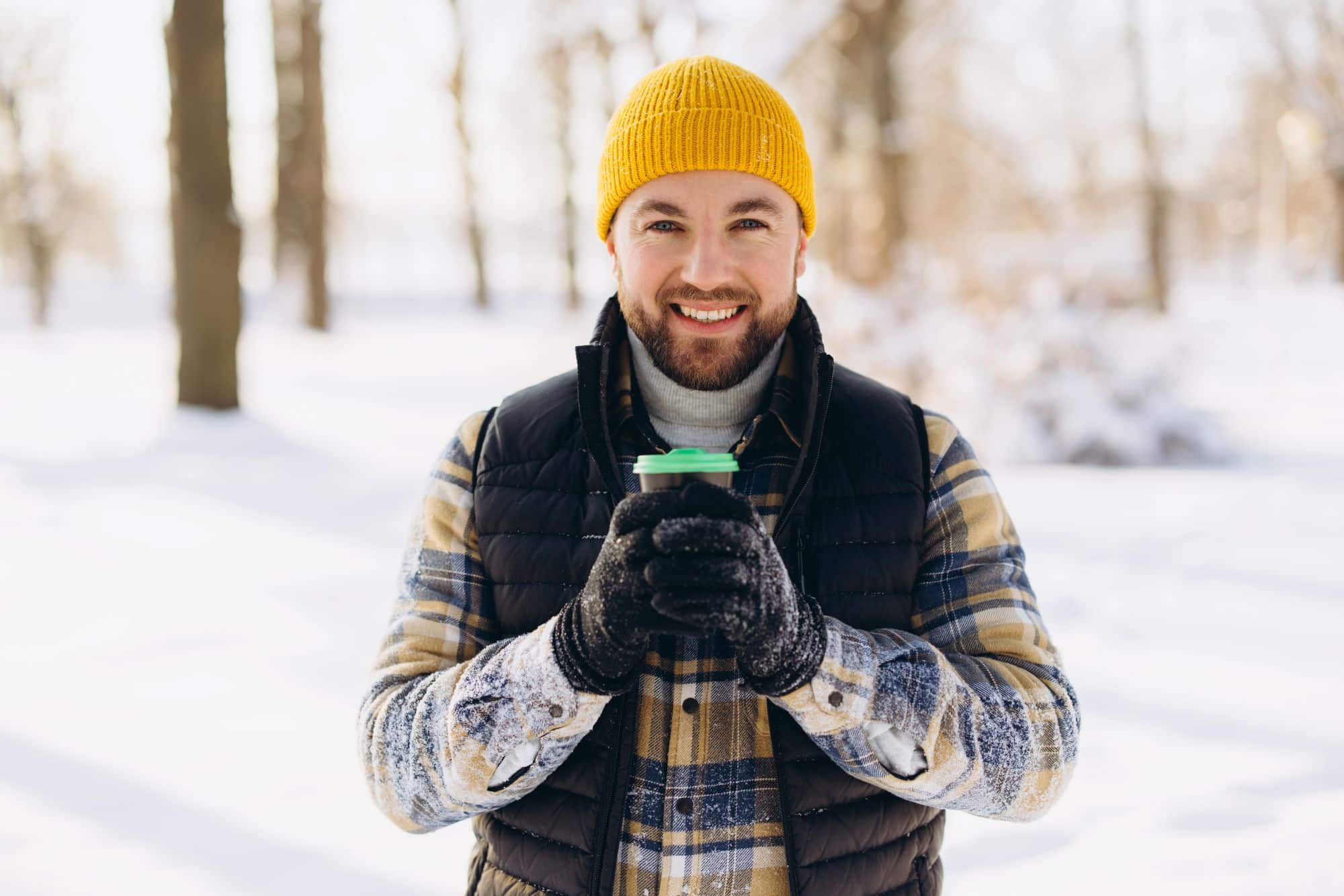 Aivoviikon 2026 teemakuva. Hymyilevä mies katsoo kameraan ulkona talvisessa maisemassa. Miehellä on keltainen pipo ja lunta vaatteissaan. Hän pitää molemmin käsin pahvisesta kahvikupista.