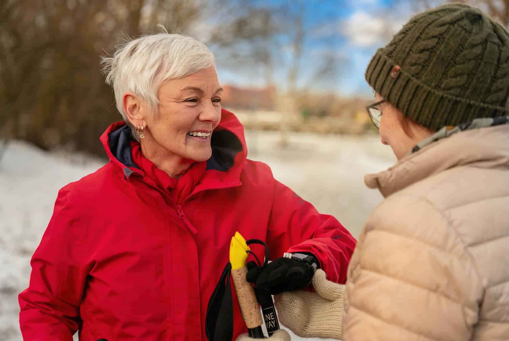 Kaksi naista ulkoilee talvisessa maisemassa. Naiset katsovat hymyillen toisiaan.